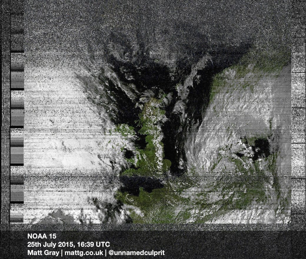 A satellite photo of the UK, with what looks like TV static fading in and out, and black and white fuzzy bars down each side. Ireland and continental Europe are mostly concealed by cloud